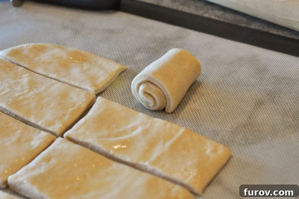 Signature Lion House Dinner Rolls 9 Several small rectangles of bread dough are shown on a cutting board, with one perfectly rolled up into an elegant snail shape.