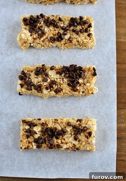 Top view of homemade chewy granola bars topped with mini chocolate chips, cut into perfect rectangles on parchment paper.