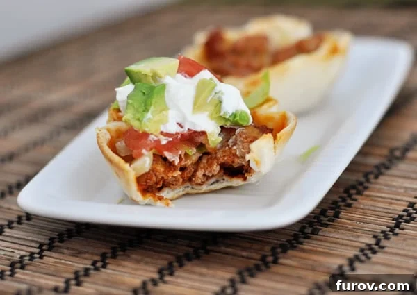 A single, perfectly baked mini taco cup with a bite taken out, resting on a clean white platter, showcasing its delicious filling.