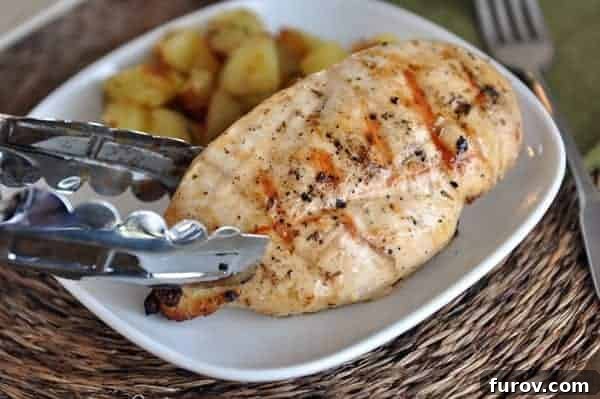 A succulent grilled chicken breast being lifted from a white plate with tongs, showcasing its perfect char and juiciness.