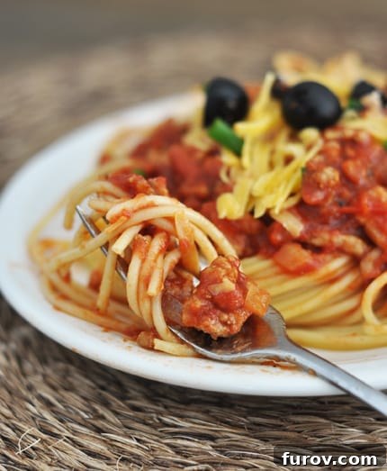 Plate full of spaghetti topped with sauce, cheese, and black olives.