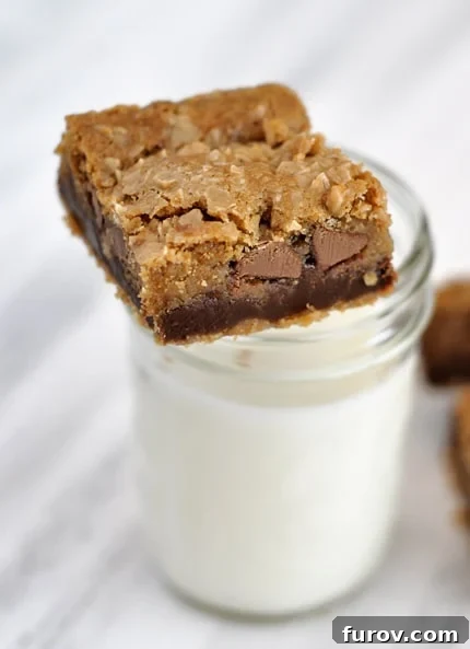 Decadent Toffee Chocolate Chip Cookie Slabs 2 A perfectly portioned fudge-filled chocolate chip cookie bar resting beside a chilled glass of milk, inviting a delightful indulgence.