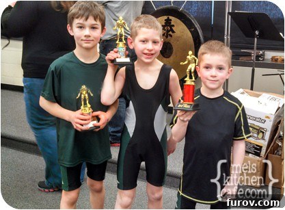 Young wrestlers proudly displaying their medals and trophies after a tournament, highlighting the positive impact of inclusive recognition.