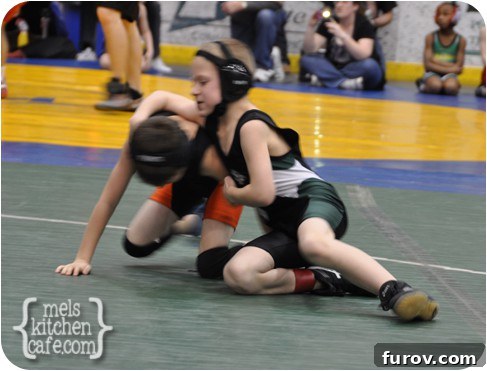 A young wrestler executing a move on the mat during a match, illustrating the intensity and detail parents often wish to capture on video.