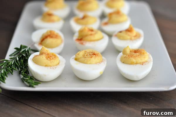 Top view of a white tray of deviled eggs with a sprig of rosemary on the side, highlighting their perfect presentation.