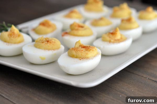 A white rectangular platter filled with perfectly arranged deviled eggs, garnished with paprika.