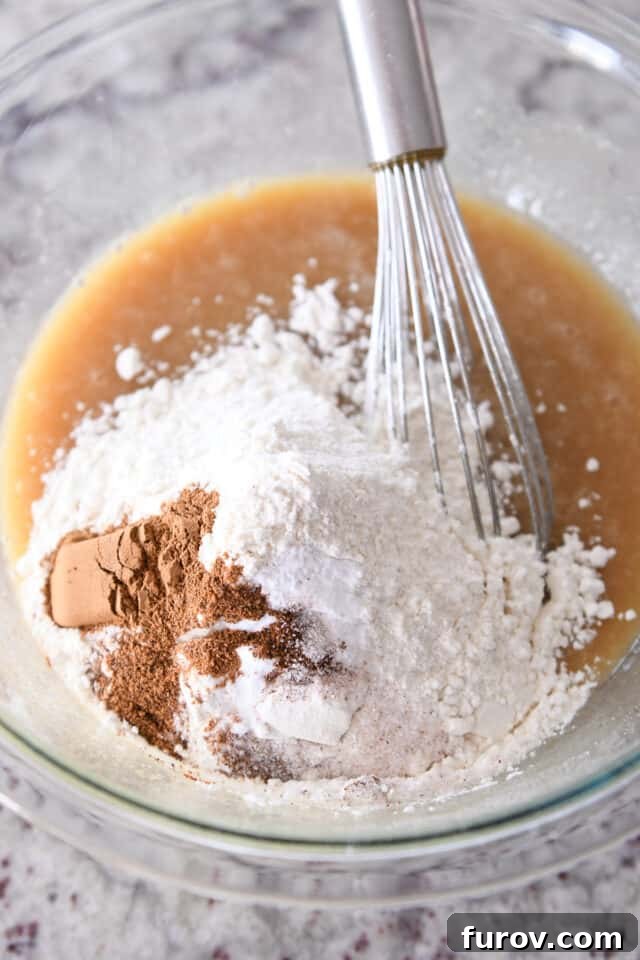 A glass bowl containing a rich carrot cake batter, with visible specks of flour, cinnamon, and a pinch of salt, showcasing the well-combined dry ingredients within the wet mixture.