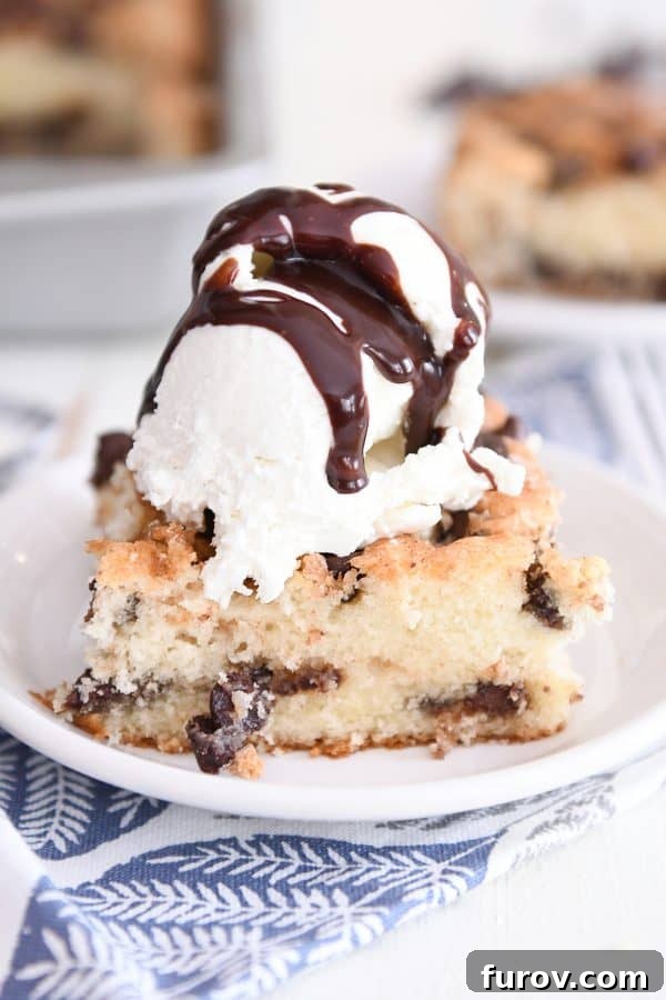 A delightful piece of one bowl chocolate chip cake served on a white plate, accompanied by a scoop of vanilla ice cream and drizzled with warm hot fudge sauce.