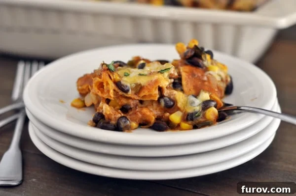 A generous serving of cheesy Tex-Mex enchilada casserole, garnished with fresh cilantro, on a white plate with a fork, ready to be eaten.