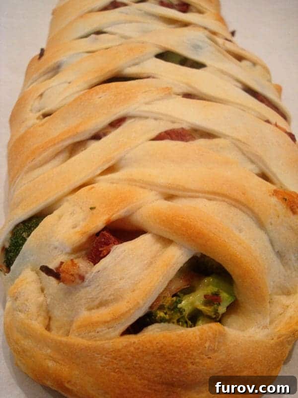 Golden brown crescent braid filled with visible ham and broccoli peeking through, artfully crisscrossed.