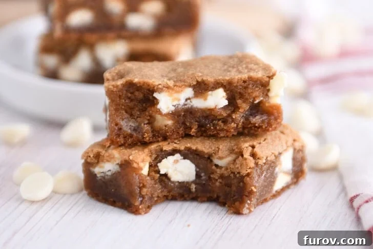 Two squares of white chocolate gingerbread blondie bars stacked with a bite taken out of the bottom bar, showcasing their soft, chewy texture.