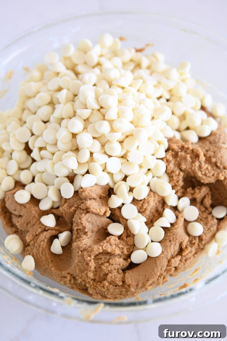 Glass bowl filled with gingerbread cookie batter studded with generous white chocolate chips, ready for baking.