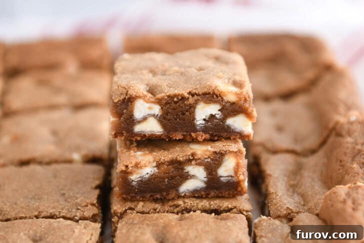 Two squares of gingerbread white chocolate blondie bars stacked, showing off their rich, golden interior and visible white chocolate chunks.