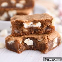 Two squares of white chocolate gingerbread blondie bars stacked with a bite taken out of the bottom bar.