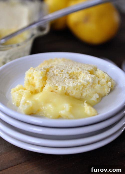 A slice of lemon pudding cake on a white plate, showcasing the two distinct layers: light cake on top and creamy pudding underneath, garnished with a sprig of mint.