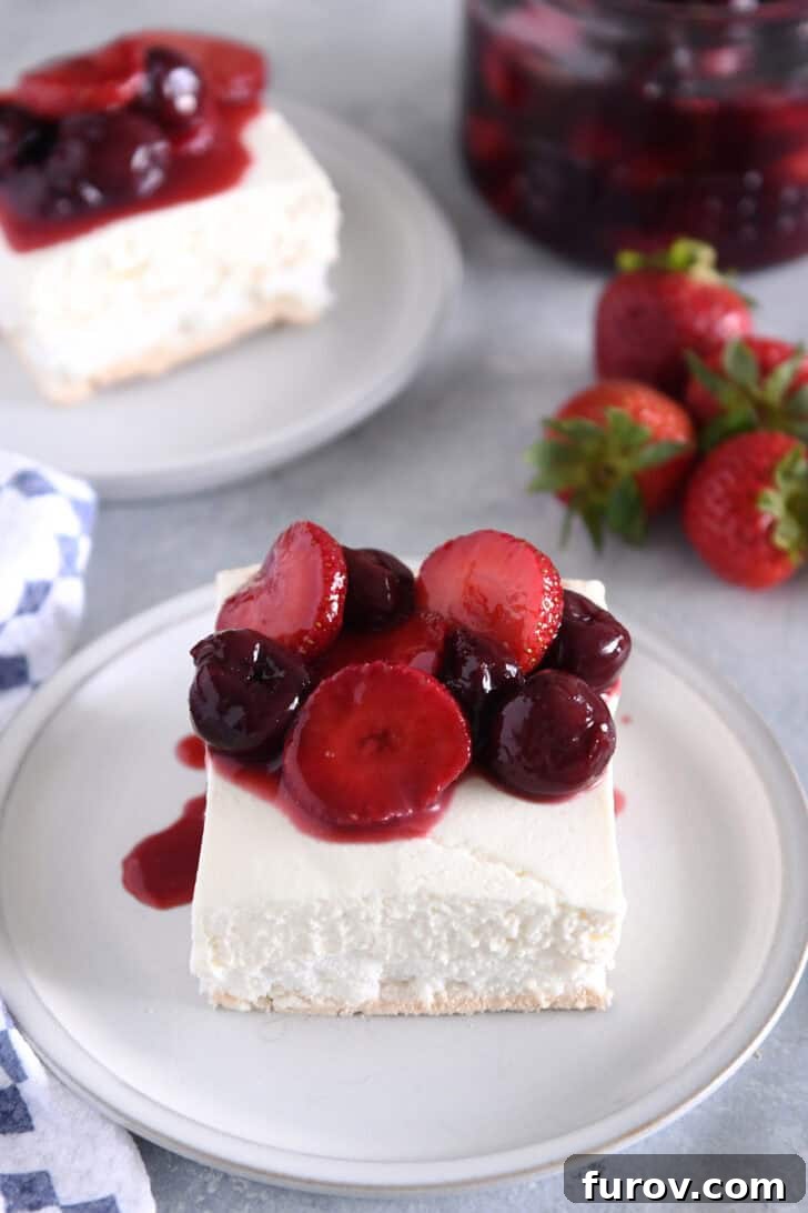 Top down view of a slice of layered meringue dessert on a white plate, generously topped with a rich berry sauce, highlighting its beautiful layers.