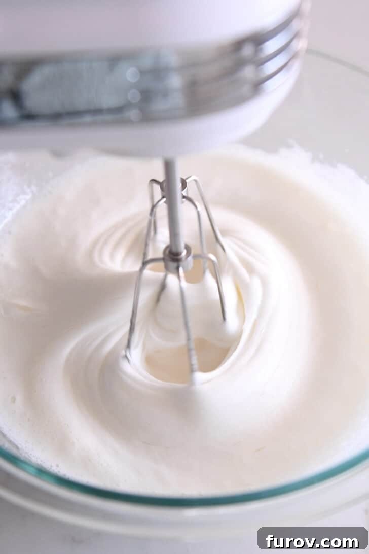 A glass bowl with a white, semi-whipped egg white mixture, showing progression towards stiff peaks, indicating good consistency.