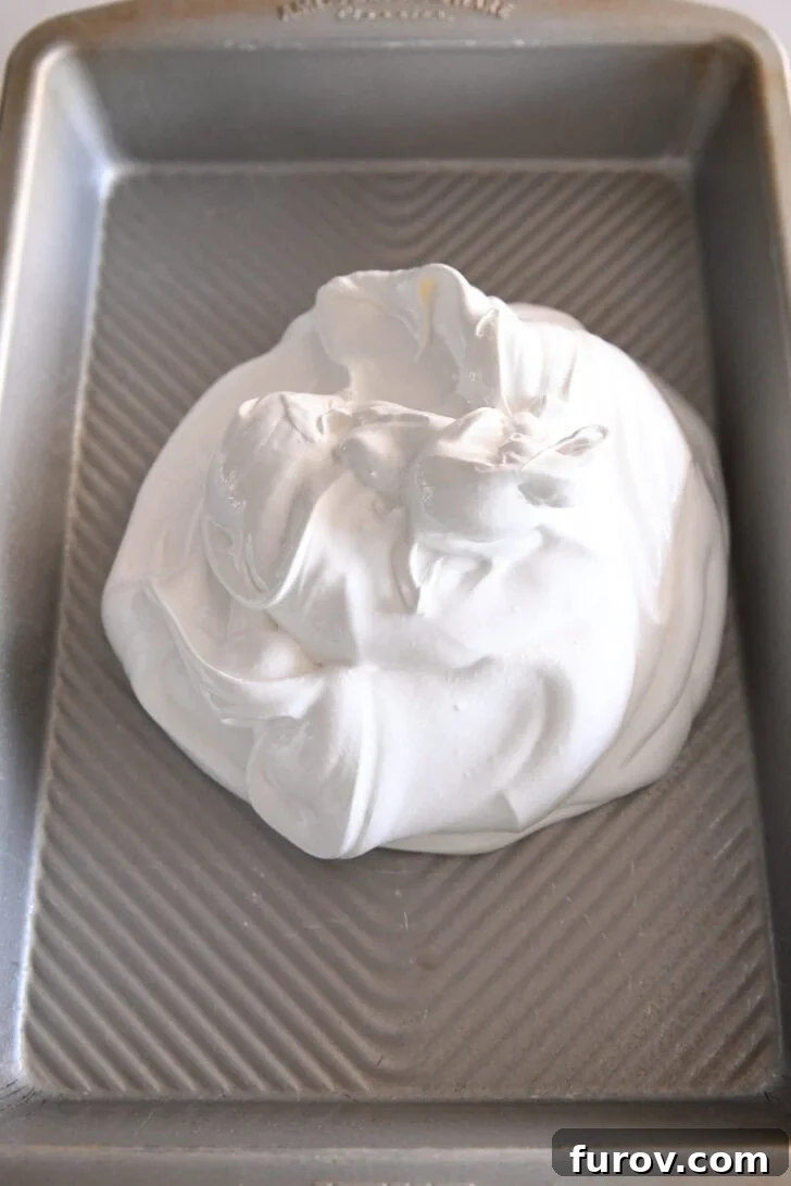 Top down view of a metal baking pan with a baked meringue base cooling in the center, showing the natural dip in the middle.
