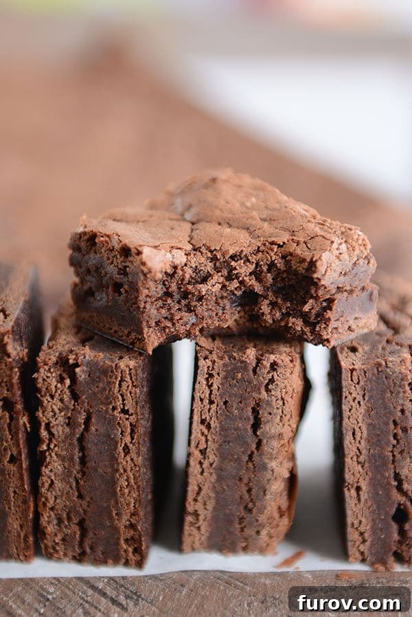 Three decadent fudgy brownies stacked artfully, with one having a bite taken out, highlighting their moist interior.