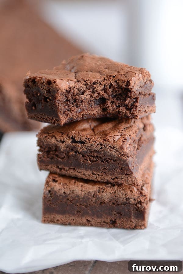 A beautifully stacked trio of fudgy chocolate brownies, with the top brownie showing a perfect bite taken out, inviting you to indulge.