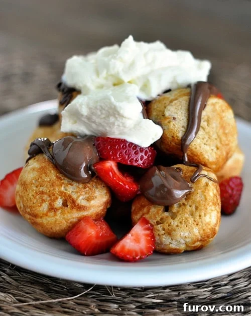 Plate full of golden brown ebelskivers topped with sliced strawberries, chocolate sauce, and whipped cream. Learn how to make these fluffy Danish pancakes and create your own breakfast masterpiece!