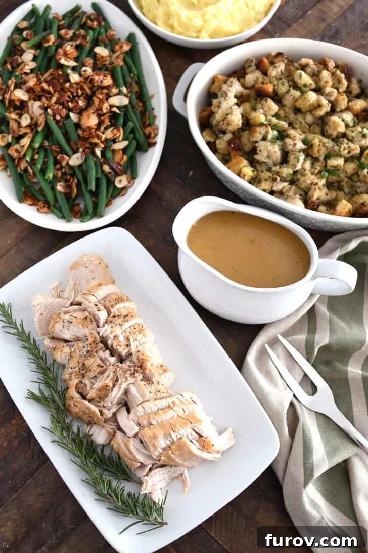 Top down view of platters of turkey, rosemary, gravy, stuffing, green beans and mashed potatoes.