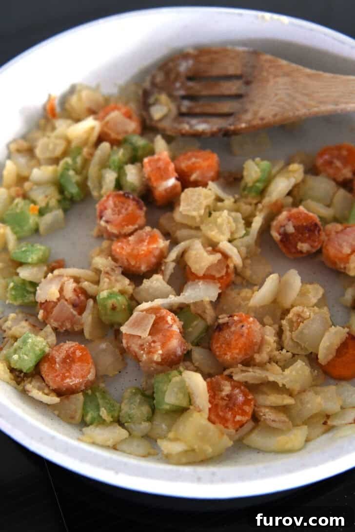 White skillet with wooden spoon and flour-coated carrots, celery and onions.