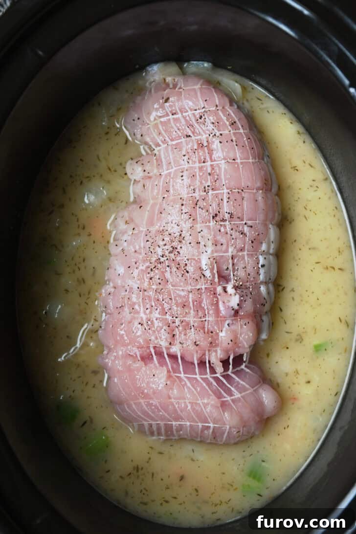 Top down view of turkey breast in slow cooker with broth and veggies.