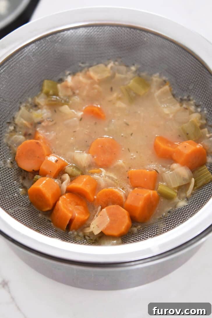 Fine mesh strainer over saucepan with cooked carrots, celery and broth mixture.