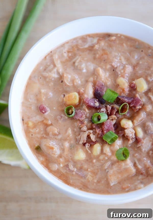 A vibrant, creamy slow cooker jalapeno popper white bean chili in a white bowl, generously topped with crispy bacon and fresh chives, ready to be enjoyed.