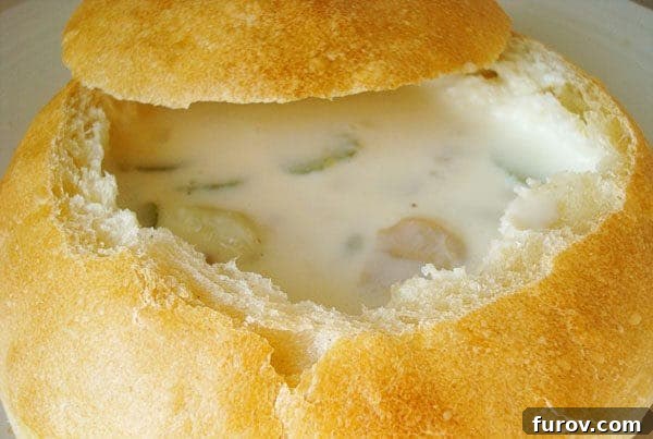 Hearty clam chowder, garnished with fresh green herbs, filling a crusty homemade bread bowl.