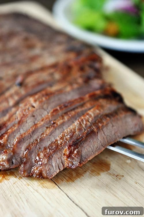 A perfectly grilled flank steak, expertly sliced into thin strips on a rustic wooden cutting board, ready to be served. 
