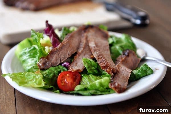 Tender, thinly sliced grilled steak strips arranged on a fresh green salad, highlighting the versatility of the recipe.