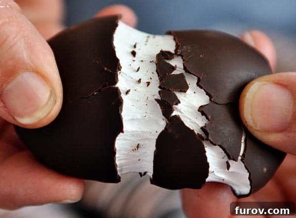 Hands pulling apart a chocolate marshmallow egg to reveal the fluffy interior.