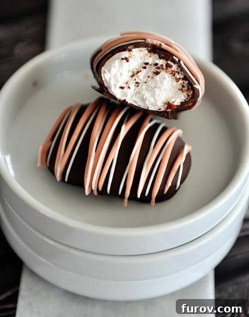 Two chocolate covered and chocolate drizzled marshmallow eggs on white plates, one with a bite taken out.