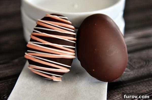 Two chocolate covered marshmallow Easter eggs sitting against a stack of white plates.