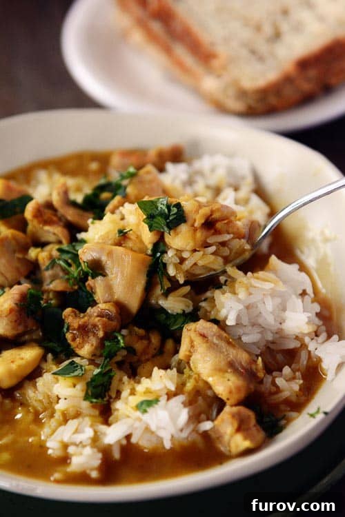 A spoon taking a bite out a bowl of white rice and chicken curry, garnished with fresh cilantro.