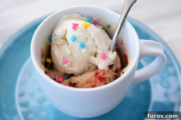 A beautiful top-down shot of a white mug filled with a perfectly baked funfetti cake, generously topped with a scoop of vanilla ice cream, ready to be enjoyed.