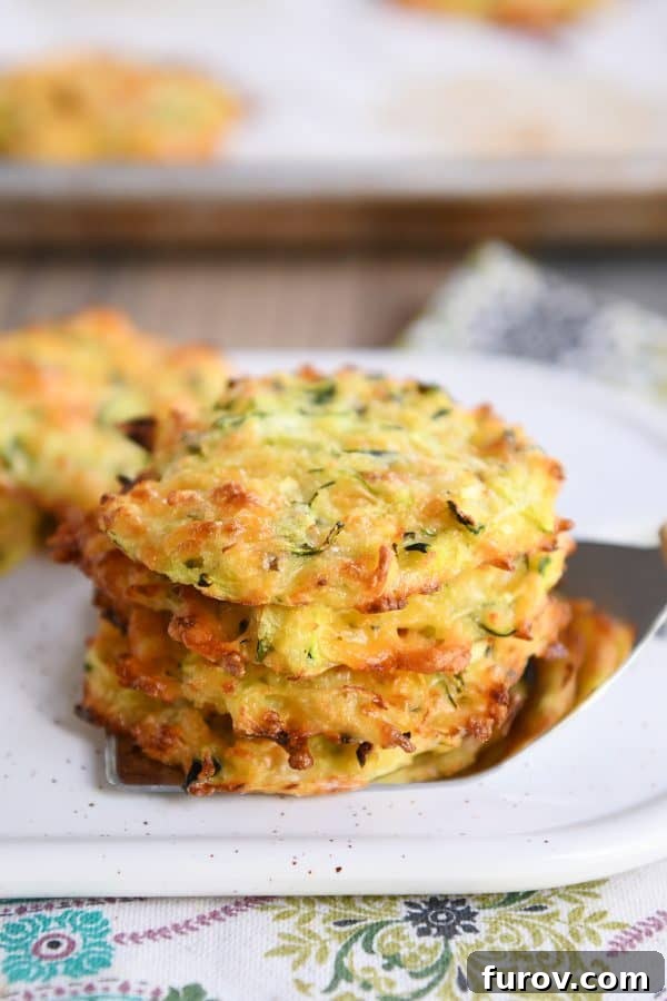 Four golden-brown baked cheesy zucchini bites, perfectly stacked on a serving spatula, showcasing their crispy edges and inviting texture.