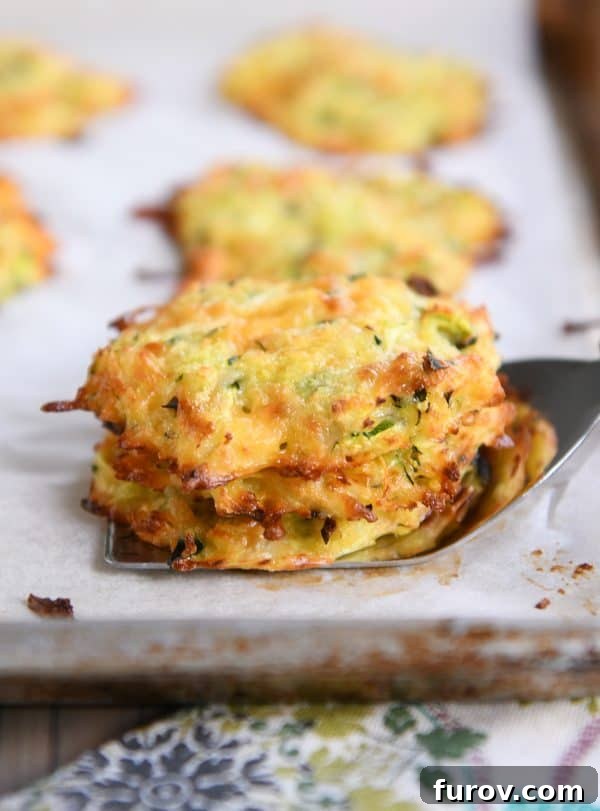 Two baked cheesy zucchini bites balanced on a serving spatula, showcasing their appealing golden-brown crust and inviting texture, ready for serving.