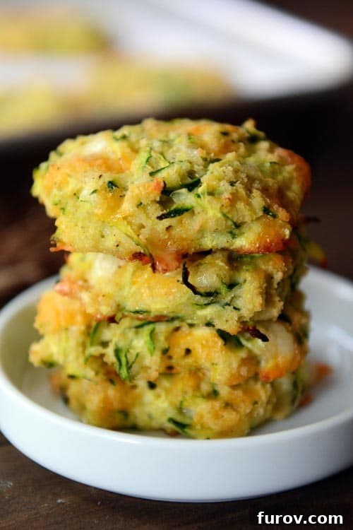Four golden-brown Baked Cheesy Zucchini Bites, artfully stacked on a small white ramekin, highlighting their delicious appearance and serving potential.