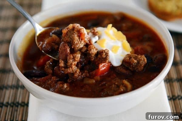 Slow-Simmered Comfort Chili 9 A white bowl of beef chili with sour cream and cheese on top.