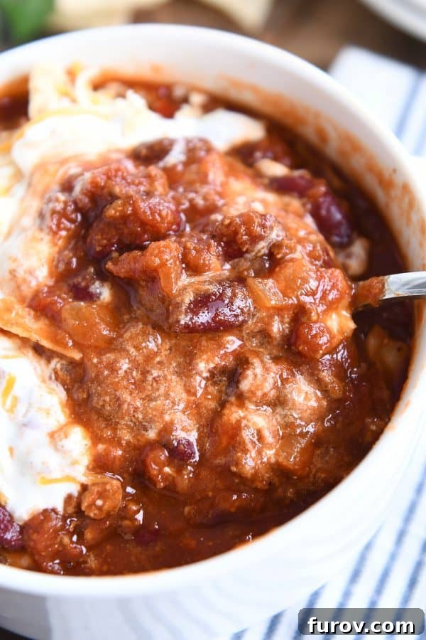 Slow-Simmered Comfort Chili 7 Taking a spoonful of classic slow cooker chili out of a white bowl.