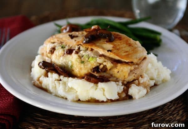 Homemade Stuffed Chicken Marsala 3 A white plate featuring a perfectly stuffed chicken breast atop a bed of creamy mashed potatoes, garnished with vibrant green beans, creating a gourmet presentation.