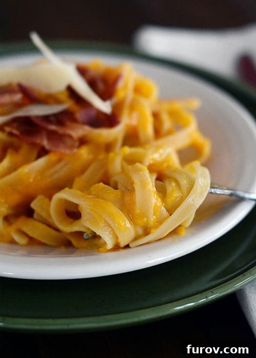 Velvet Butternut Bacon Pasta 2 A white plate with cooked linguine pasta topped with bacon and parmesan cheese, garnished with fresh herbs.