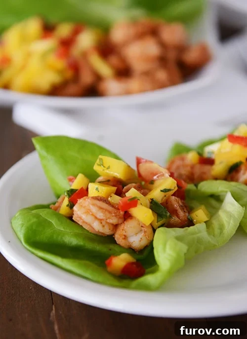 Vibrant shrimp and mango lettuce wraps beautifully arranged on a white plate, showcasing fresh ingredients and appealing colors.
