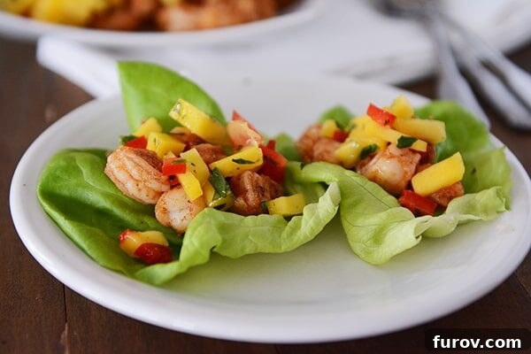 Two perfectly assembled shrimp and mango lettuce wraps resting on a pristine white plate, ready to be enjoyed.