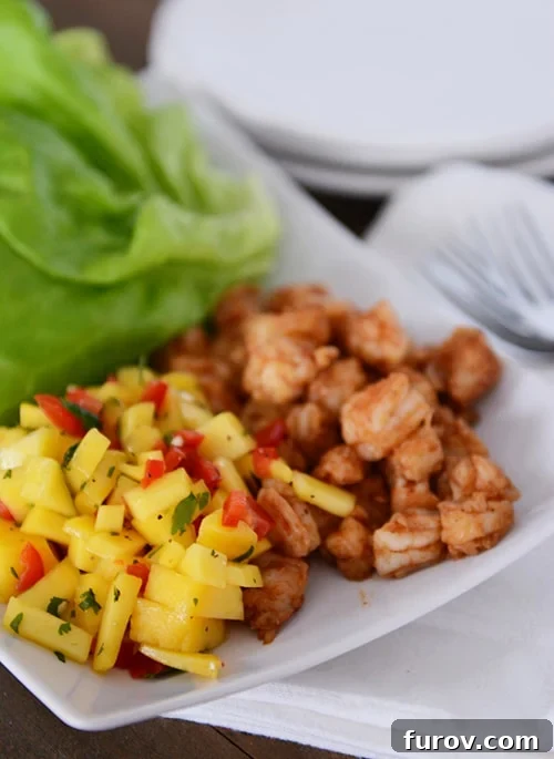 A beautifully presented white platter featuring expertly cooked shrimp on one side and a vibrant, freshly chopped mango salsa on the other, inviting creation of delicious wraps.