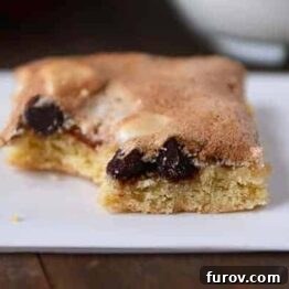 A meringue-topped chocolate chip bar with a bite taken out, revealing the cookie base and chocolate chips.