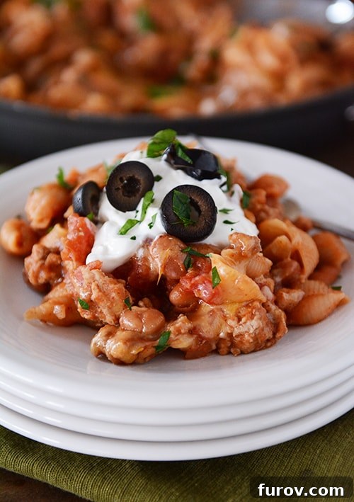 A stack of pristine white plates, each with a generous helping of cheesy taco pasta shells and fresh cilantro garnish.